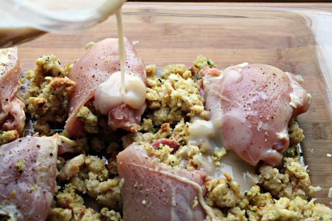 Gravy is being poured over the raw stuffed chicken in a glass casserole dish.