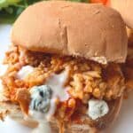 Close up view of one buffalo chicken slider with chunks of blue cheese and dressing dripping down the front of the sandwich.