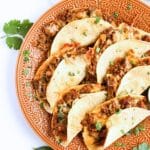 Six prepared baked tacos on a serving dish.