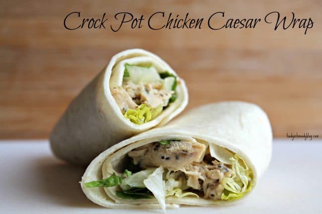 A prepared and assembled chicken caesar wrap on a white board. The wrap has been cut in half revealing the chicken and lettuce.