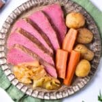 Aerial view of a rustic looking plate holding six slices of prepared corned beef, three carrots, four baby potatoes and a scoop of cooked cabbage.