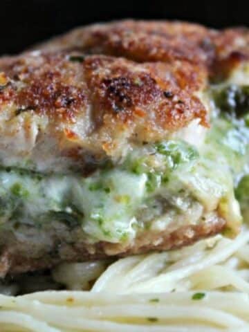 close up of stuffed pork chop. The filling is oozing out of the center and it sits upon a bed of pasta.