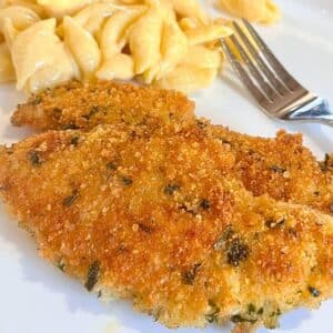 Two crispy chicken tenders on a white plate with mac and cheese next to it.