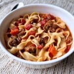 Prepared sausage soup in a white bowl. the bowl is on a tan colored background.