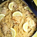 Overhead view of prepared chicken and rice still in a skillet. The food is topped with lemon slices.