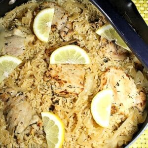Overhead view of prepared chicken and rice still in a skillet. The food is topped with lemon slices.