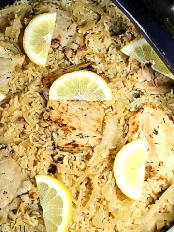 Overhead view of prepared chicken and rice still in a skillet. The food is topped with lemon slices.