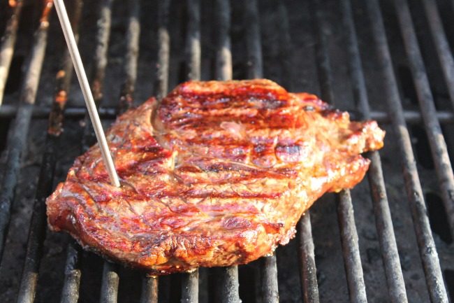 steak on grill grates cooking with thermometer sticking out of steak
