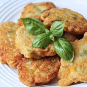 Close up of a pile of prepared zucchini flower fritters topped with fresh basil leaves.