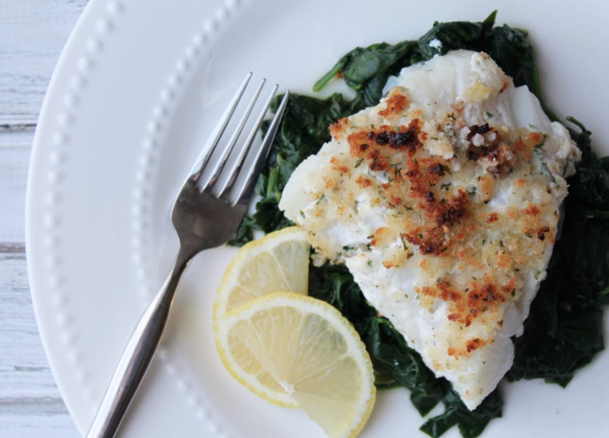 crispy topped fish on plate with spinach and lemon slices on plate