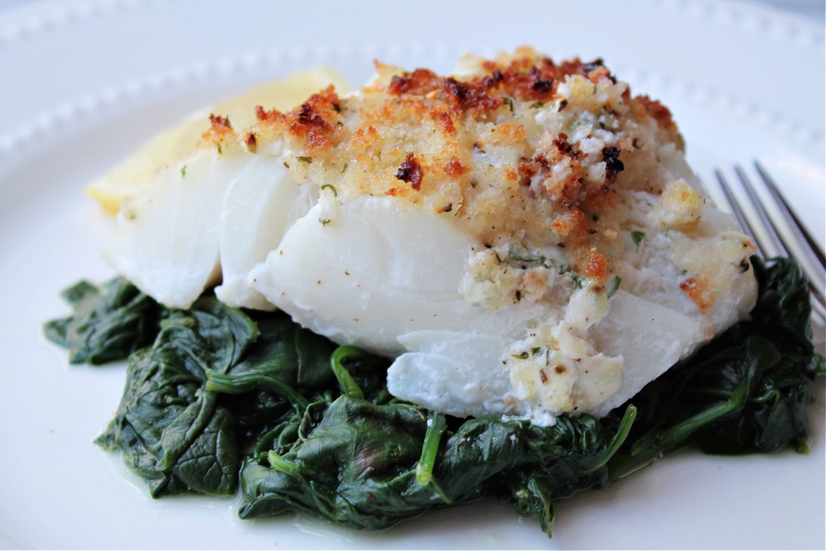 baked cod on a bed of spinach on white plate