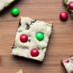 A single m&m cookie bar on a wooden background. There are red and green m&m candies scattered around it.