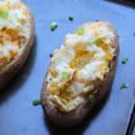 Two prepared twice baked potatoes on a dark colored baking sheet.