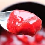 Close up of strawberry sauce on a spoon. You can see the blurred strawberry sauce bowl in the back.