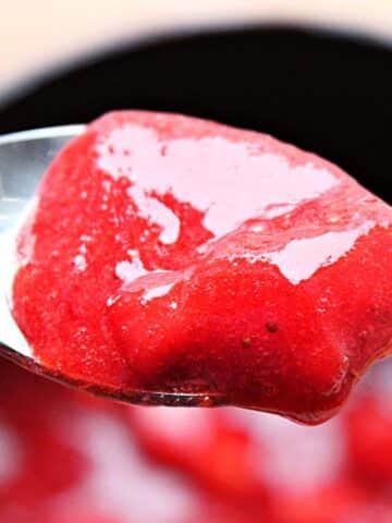 Close up of strawberry sauce on a spoon. You can see the blurred strawberry sauce bowl in the back.