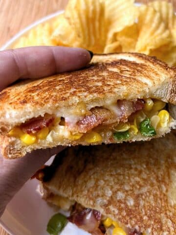 Hand holding up half of a bacon corn grilled cheese.