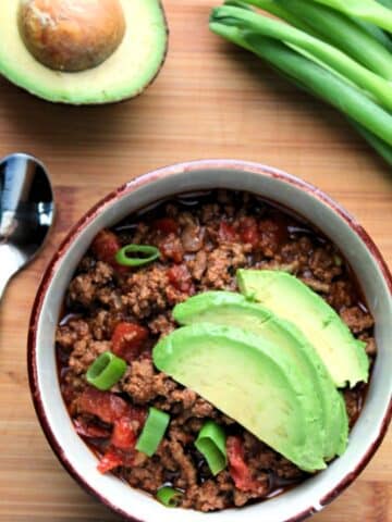 bowl of prepared chili topped with sliced avocado.