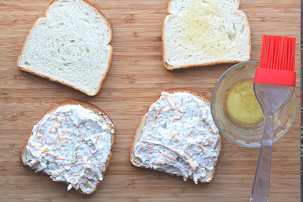 cream cheese mixture spread on two slices of bread with melted butter in bowl next to them.
