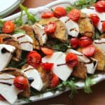 Close up view of eggplant caprese salad put together and on a white platter.
