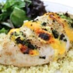 Close up of cooked and crispy cheesy broccoli chicken. The chicken is on top of couscous and you can see greens to the left.