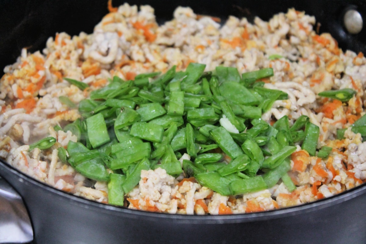skillet with browned chicken, cooked carrot and snow peas