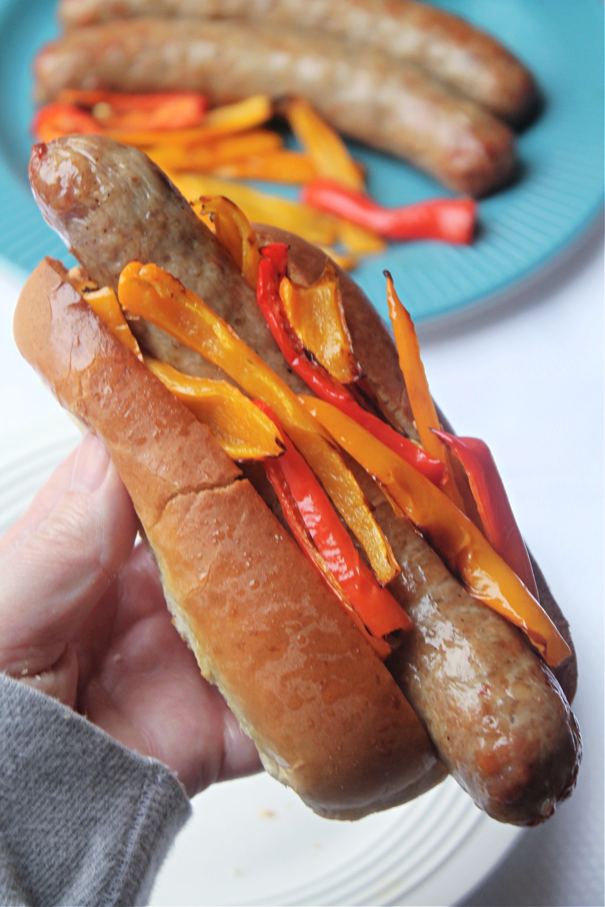 sausage in roll with peppers being held in hand