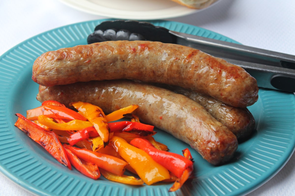 3 sausage cooked on blue plate with peppers and tongs