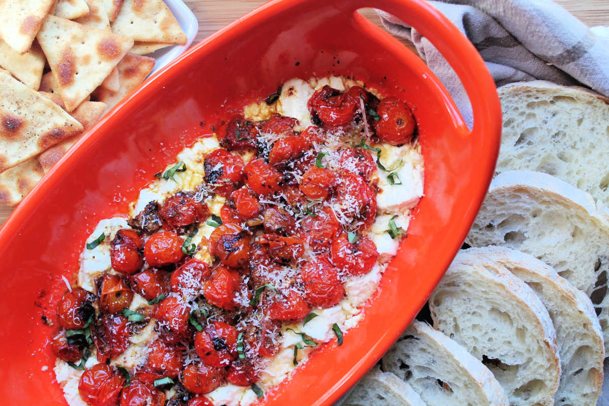 tomato dip baked and in orange serving platter, surrounded by pita chips and sliced bread