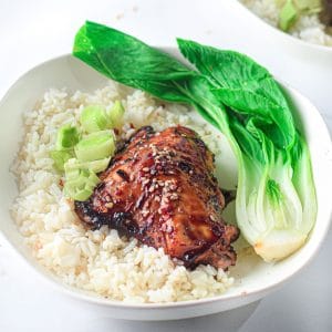 asian-glazed chicken thigh in a white bowl with white rice and steamed bok choy, garnished with sliced green onion