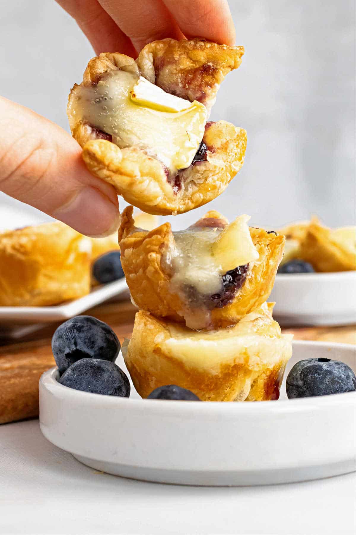 stacked baked brie puffs on small white plate. A hand is taking the one off the top.
