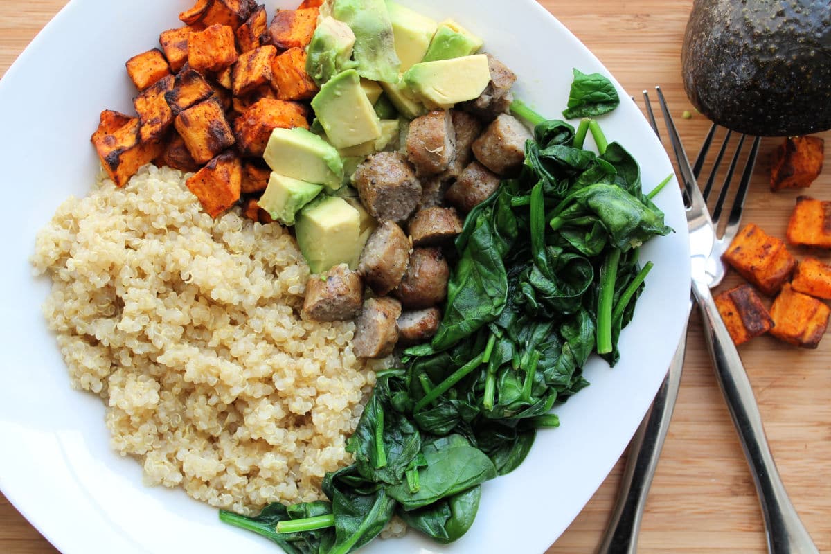 white bowl filled with quinoa, spinach, sausage, sweet potatoes and avocado.