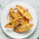 air fryer garlic bread stacked on a white dish on a white speckled counter top