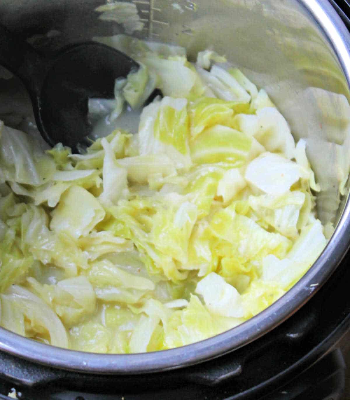 cooked cabbage in pot. A black serving spoon is stirring it.