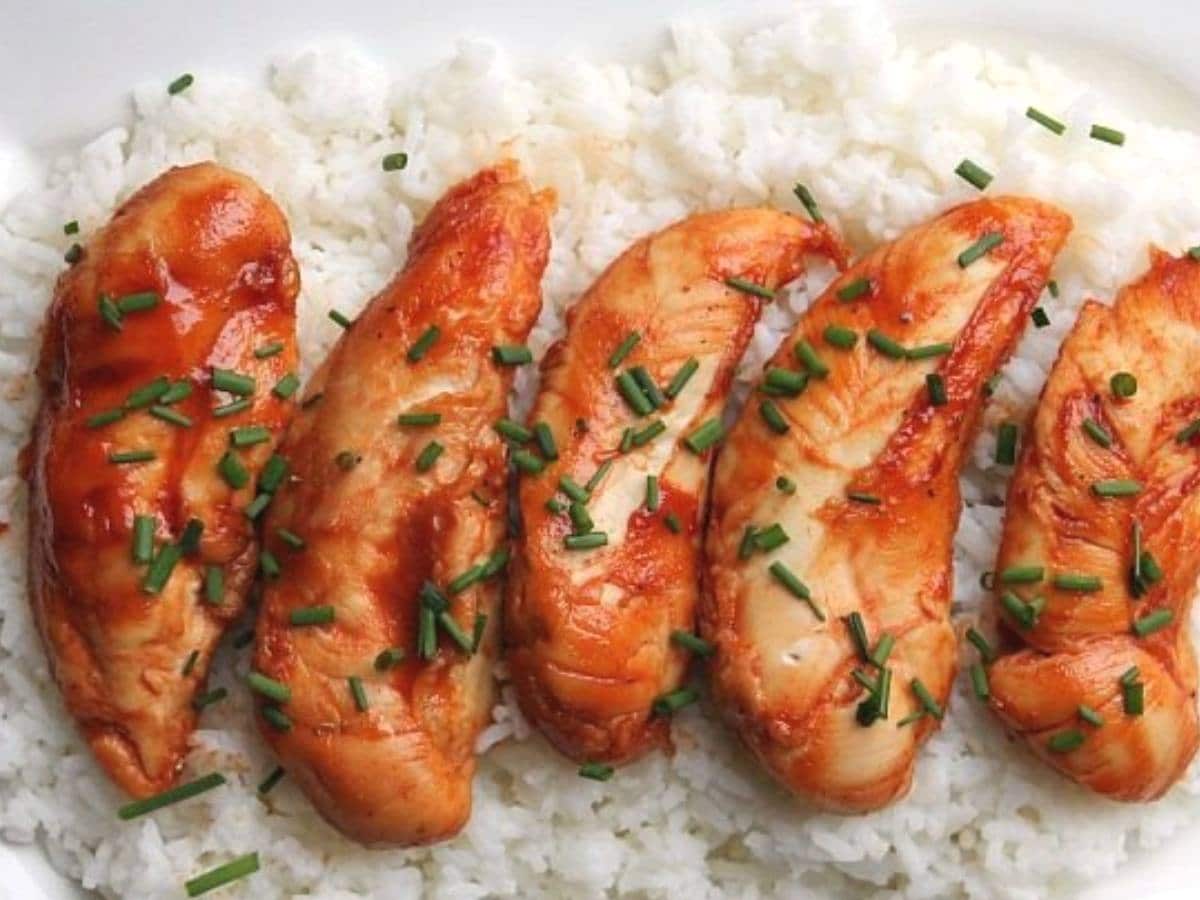 close up photo of five cooked chicken tenders of a bed of white rice. the chicken is topped with chopped chives.