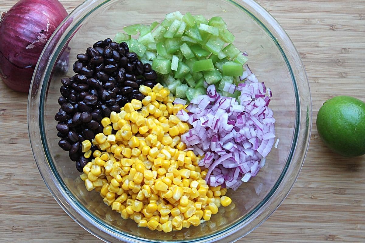 clear bowl with corn, black beans, red onion and tomatillo in it, divided into sections