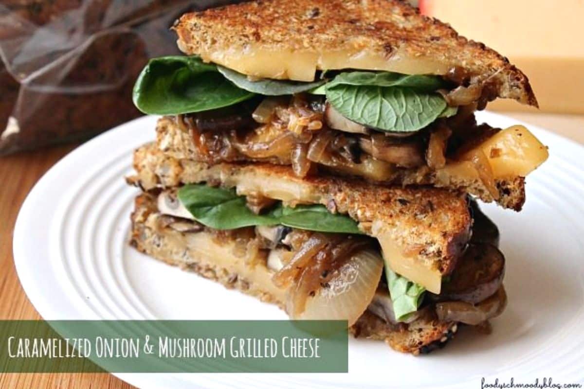grilled cheese cut in half with onions, mushrooms and spinach hanging out. The sandwich is on a white plate.