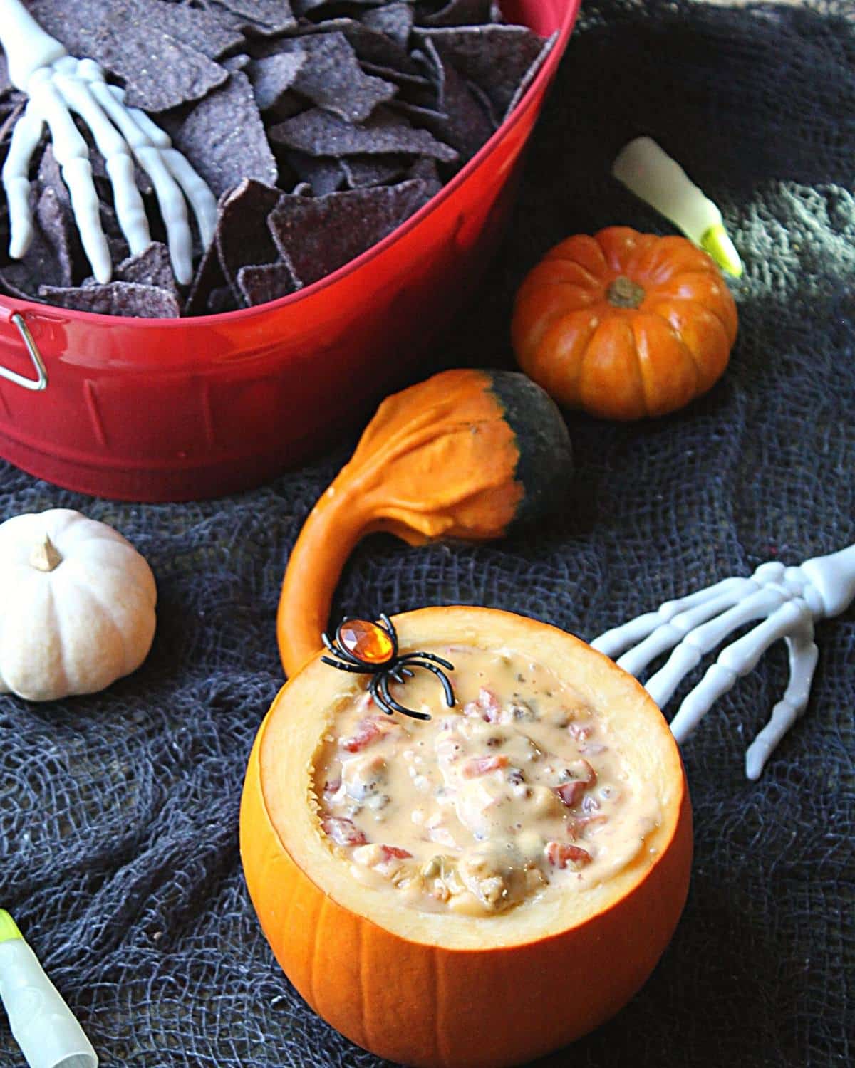 Sausage dip being served inside a hollowed out pumpkin. There is black netting and skeleton hands and mini pumpkins to set a Halloween theme.