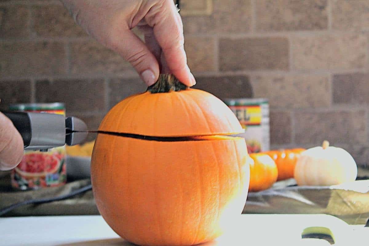Pumpkin on white cutting board with an electric knife slicing off the top.