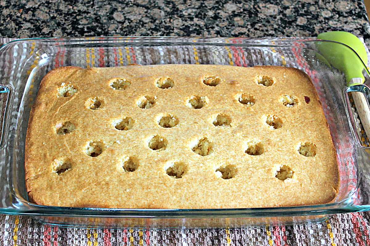 Cake baked with holes poked in it. The cake pan sits on top of a brown speckled dish towel.