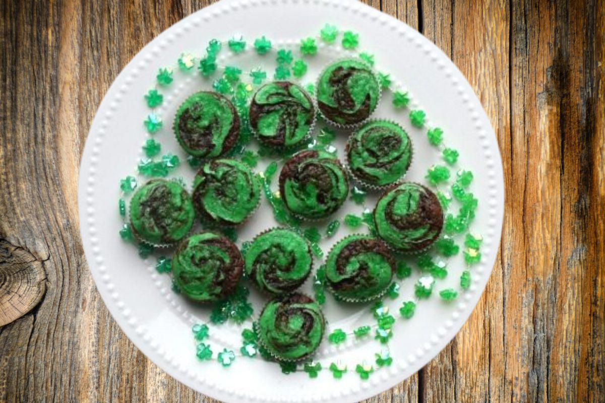A white plate on a wooden background filled with green swirled brownie bites. There is a shamrock strand all around the plate.