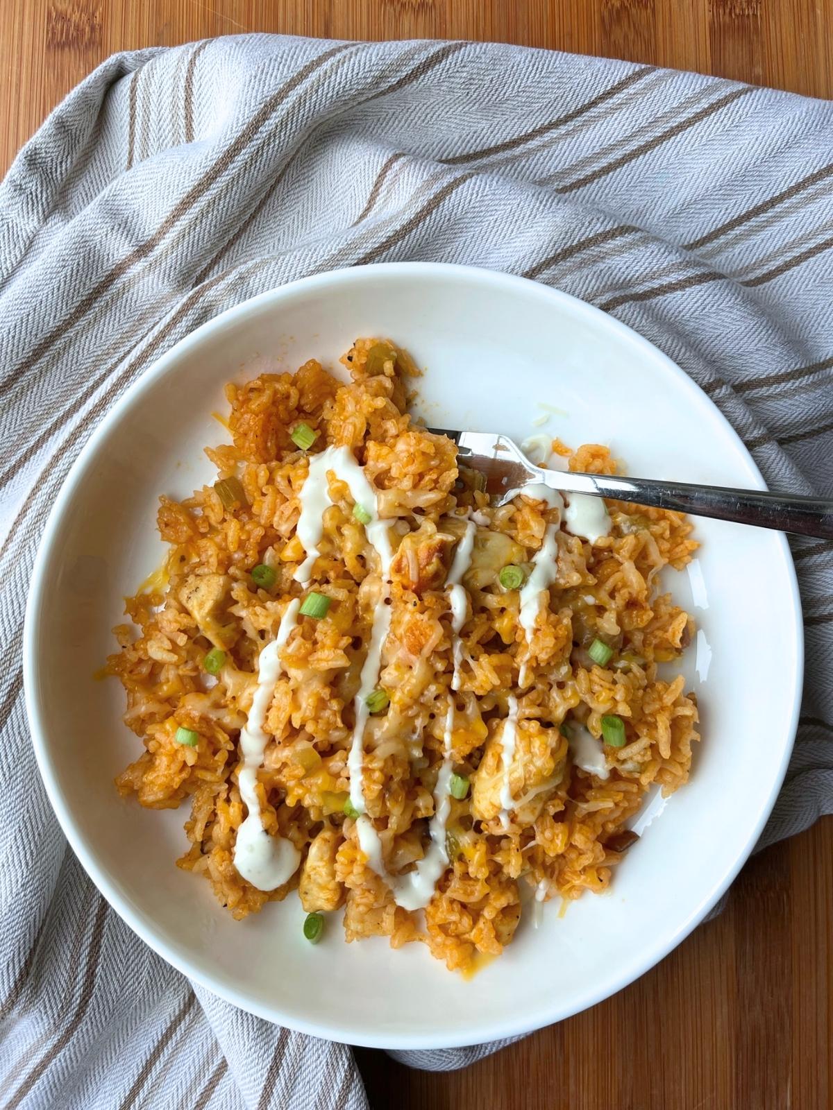 A white bowl holding the complete recipe of buffalo chicken rice. It is garnished with chopped green onions and a drizzle of ranch dressing.
