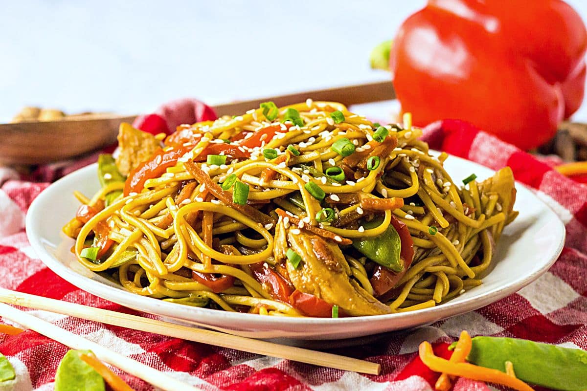 Cooked lo mein on a white plate. The plate sits on a red and white tablecloth.