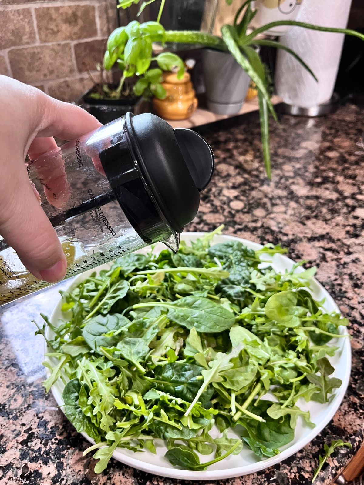 A white serving dish full of greens. There is a dressing being drizzled over the top.