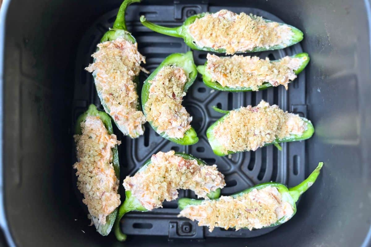 Jalapeno peppers stuffed and prepped to air fry. They are laying inside the air fryer basket but have not been cooked yet.