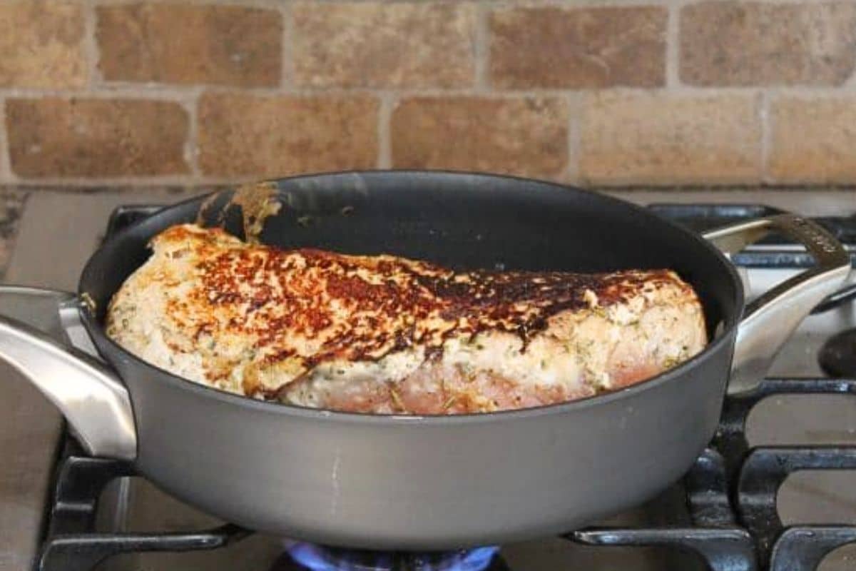 Pork loin in a large skillet on the stove. The pork appears to be browning.