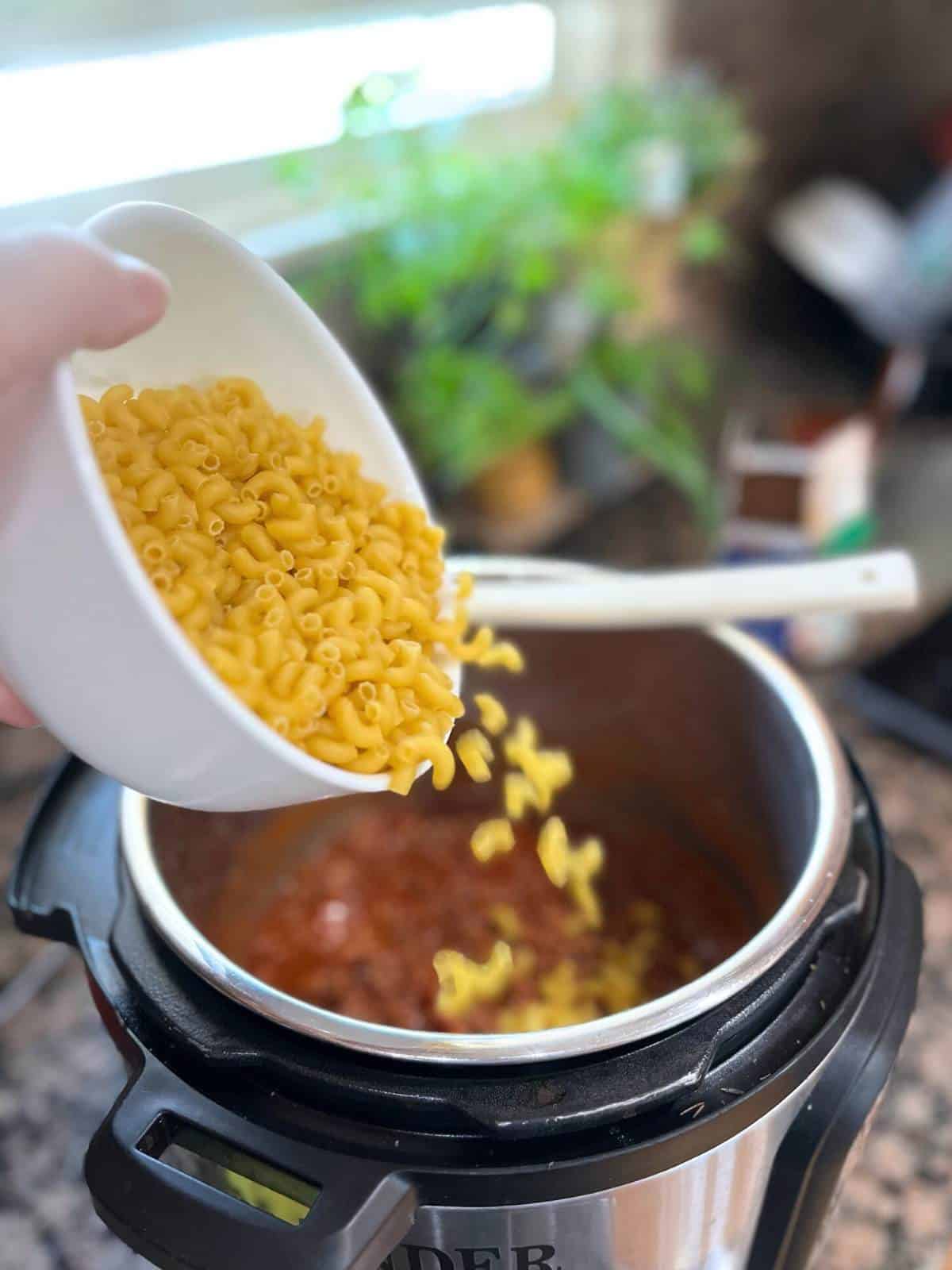 Pasta pouring from a white bowl into the instant pot.