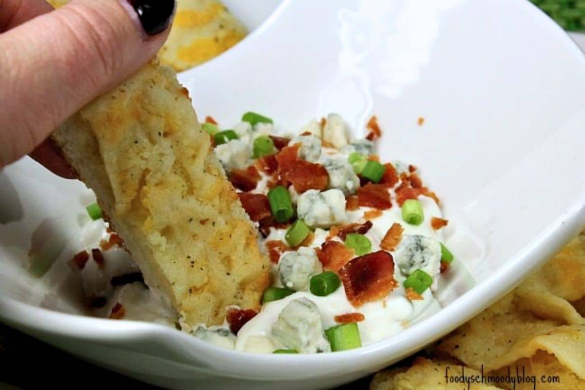 A close up of prepared dip in white bowl. There is a breadstick being dipped into it.