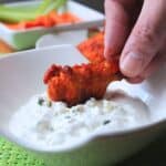A buffalo drumstick being dipped into prepared dip which is in a white bowl.