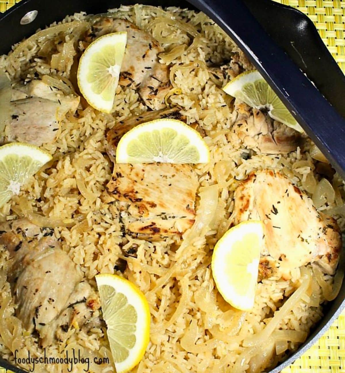 Overhead view of prepared recipe in a skillet. There are lemon slices over the chicken.