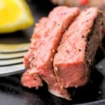 Two cuts of steak on the end of the fork. It is all on a black dish.